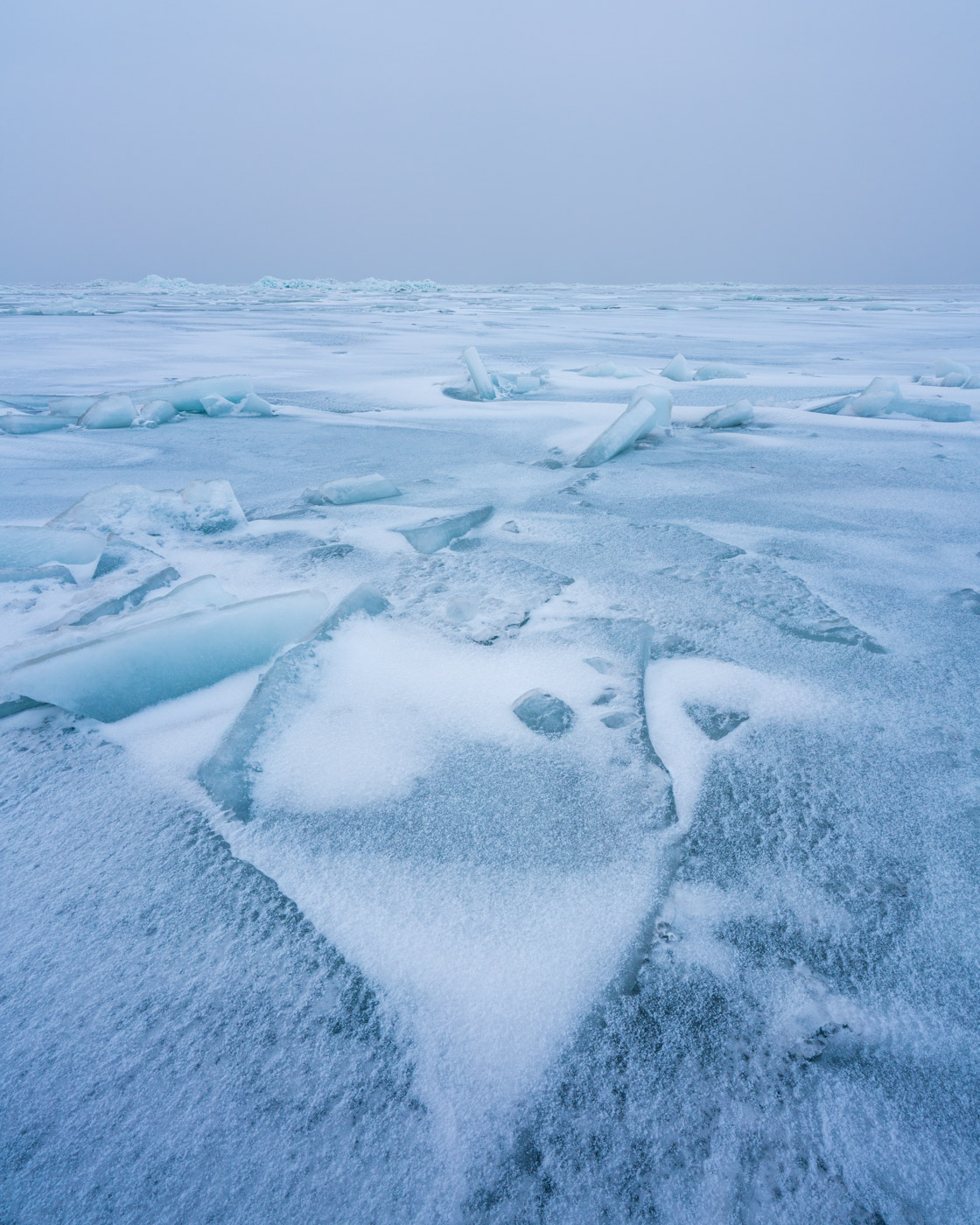 Schneebedeckte bläuliche Eisplatten reichen vom Vordergrund bis zum Horizont.
