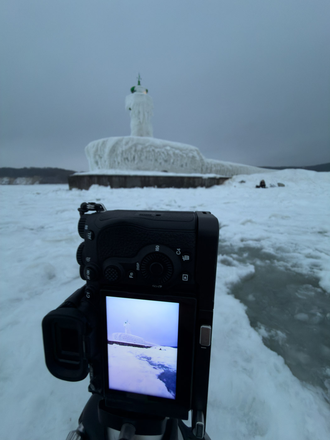 Kamera mit ausgeklapptem Display vor dem vereisten Leuchtturm.