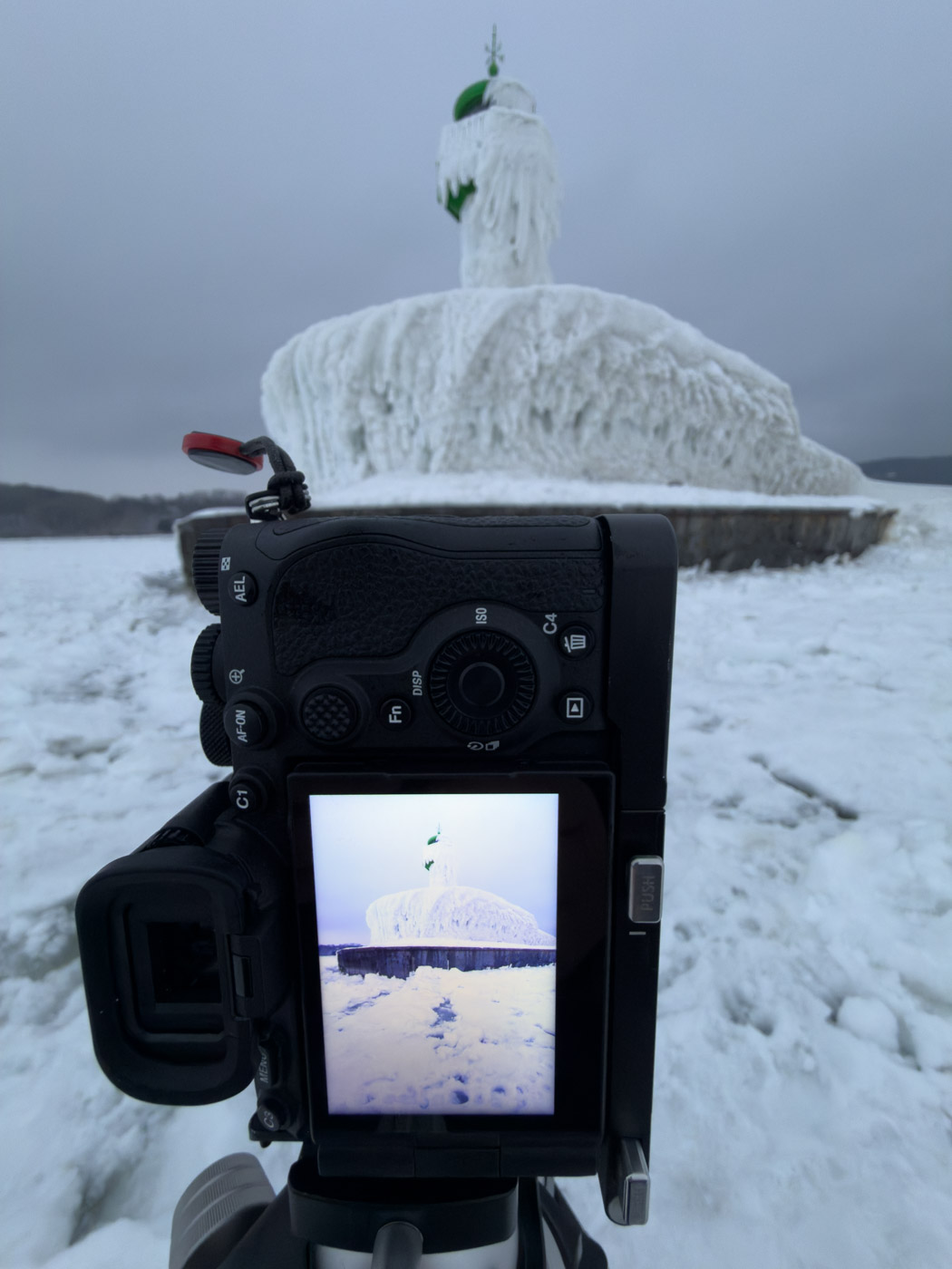 Kamera auf einem Stativ vor der eisbedeckten Mole in Sassnitz; das Motiv erscheint auf dem Display.